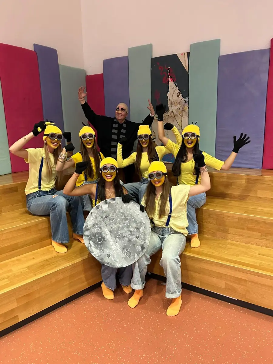 A group of dancers dressed as Minions on wooden steps, holding a painted moon